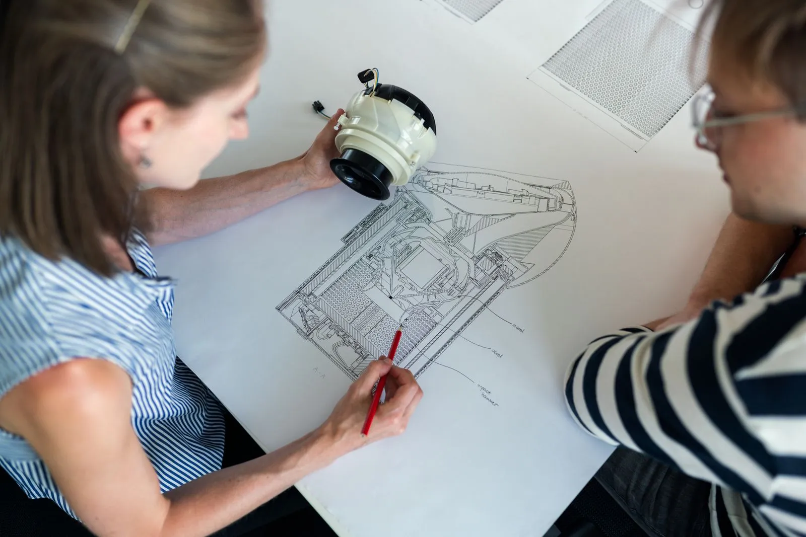 Zwei Konstrukteure besprechen eine Schnittzeichnung mit dem zugehörigen Bauteil