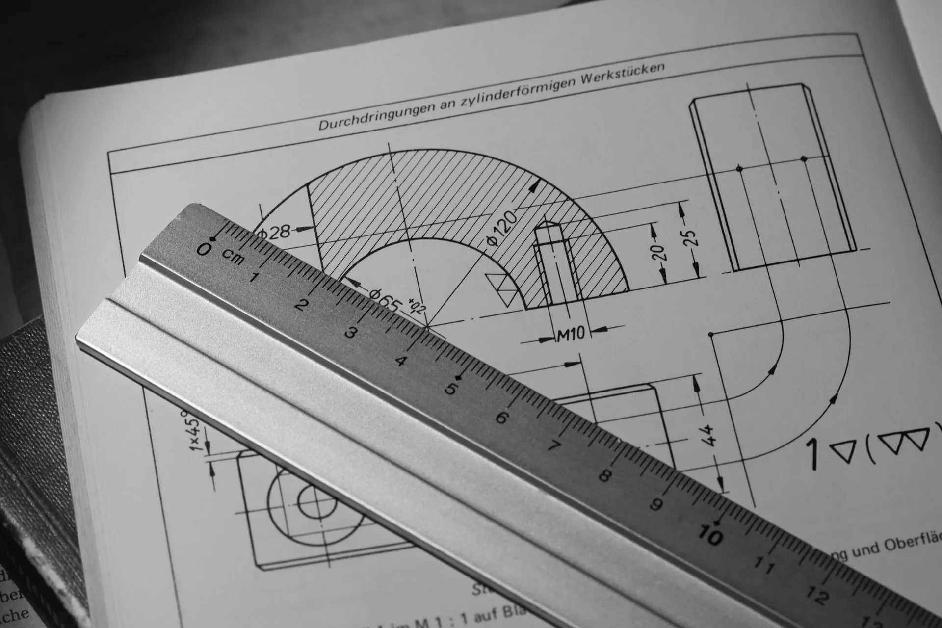 Technische Zeichnung eines zylindrischen Werkstücks mit Maßangaben, darauf ein Stahllineal